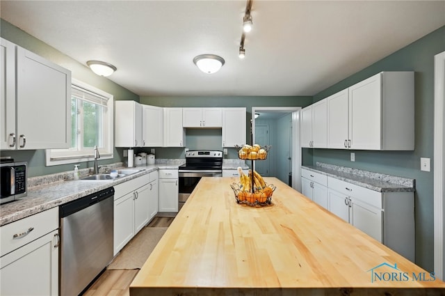 kitchen featuring white cabinets, wooden counters, stainless steel appliances, and a sink