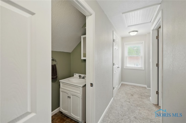 hall featuring visible vents, baseboards, dark carpet, and a sink