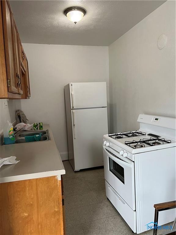 2289 Upton Ave, Toledo, OH 43606 - kitchen featuring white appliances, brown cabinets, a sink, light floors, and light countertops
