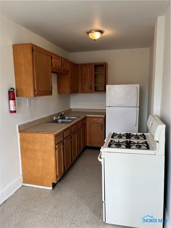 2289 Upton Ave, Toledo, OH 43606 - kitchen with white appliances, a sink, open shelves, brown cabinets, and baseboards