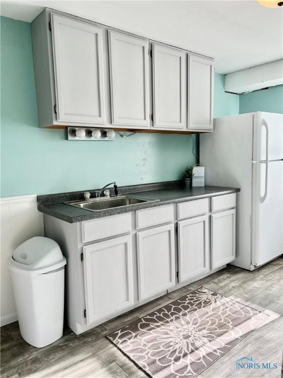 12982 State Route 34, Bryan, OH 43506 - kitchen with freestanding refrigerator, a sink, dark countertops, light wood-style floors, and wainscoting