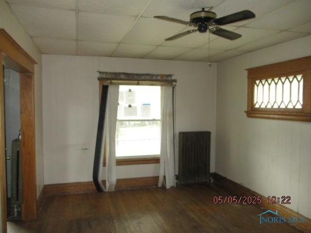 unfurnished room featuring radiator, wood finished floors, ceiling fan, a paneled ceiling, and baseboards