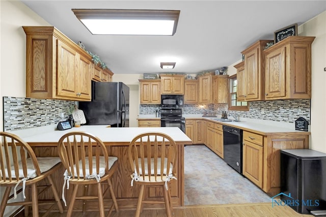 kitchen with black appliances, a sink, light countertops, a peninsula, and decorative backsplash