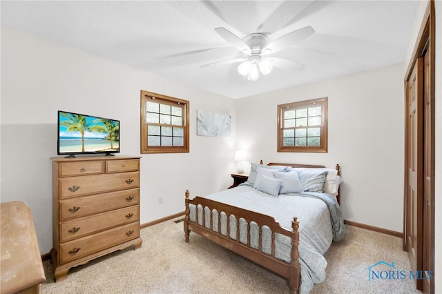 bedroom with a closet, light colored carpet, baseboards, and ceiling fan