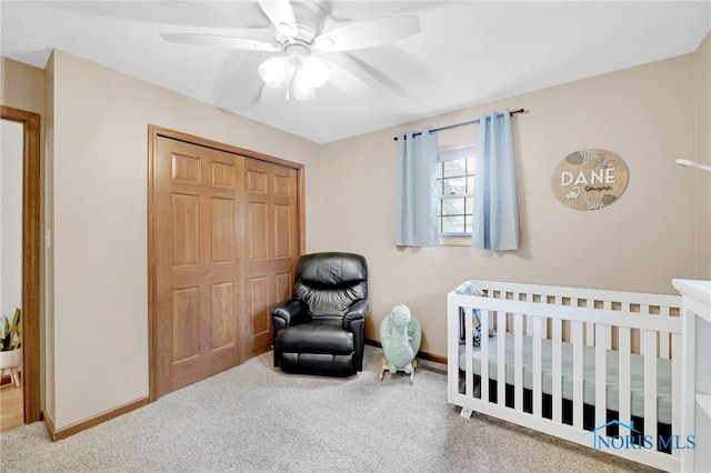 carpeted bedroom featuring baseboards, a closet, a ceiling fan, and a crib
