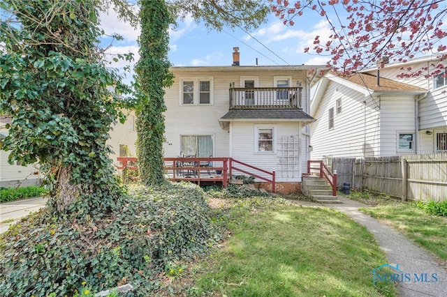back of house with a chimney, fence, a lawn, and a balcony