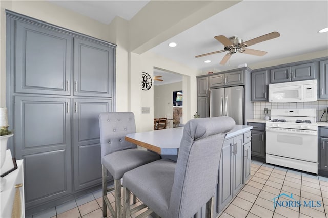 kitchen featuring white appliances, tasteful backsplash, light tile patterned flooring, a kitchen bar, and light countertops