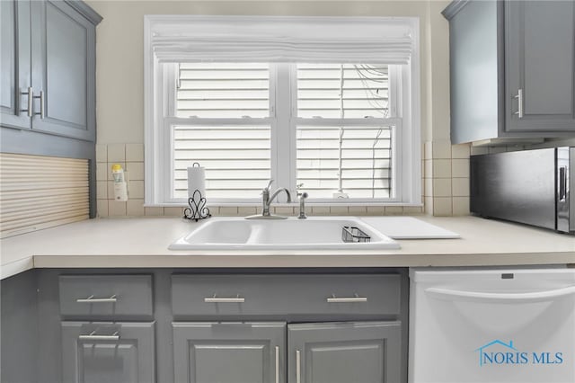 kitchen featuring backsplash, gray cabinetry, dishwasher, and a sink