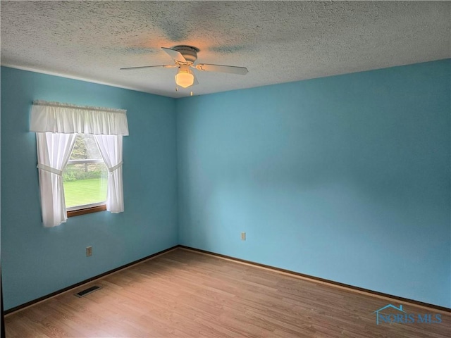 empty room with ceiling fan, a textured ceiling, visible vents, and wood finished floors
