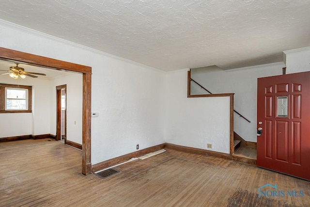 empty room featuring baseboards, ornamental molding, visible vents, hardwood / wood-style flooring, and stairway