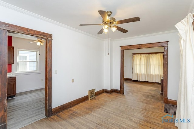 empty room with crown molding, light wood-type flooring, baseboards, and a ceiling fan