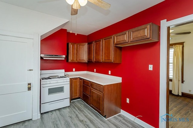 kitchen with under cabinet range hood, ceiling fan, light wood finished floors, and white gas stove