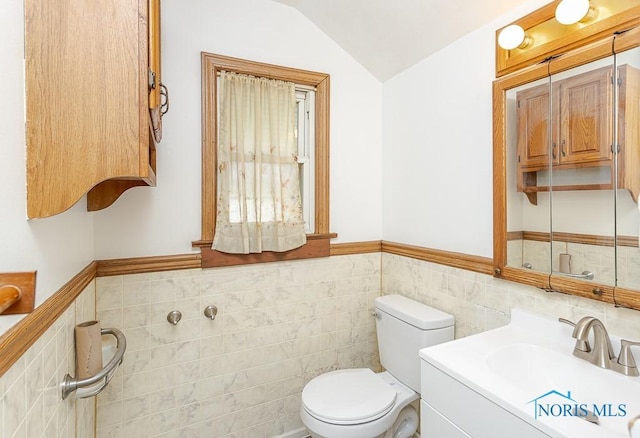 half bath with toilet, tile walls, wainscoting, vanity, and lofted ceiling