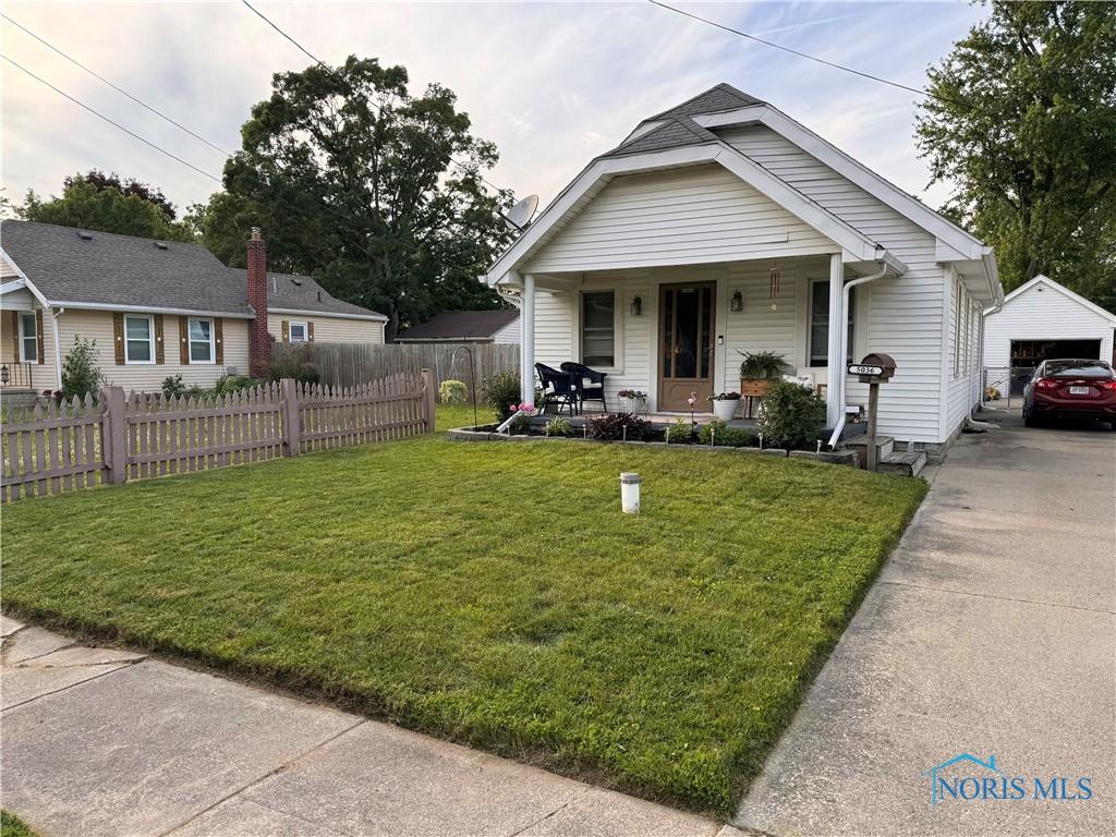 bungalow with covered porch, fence, an outdoor structure, a front yard, and a detached garage