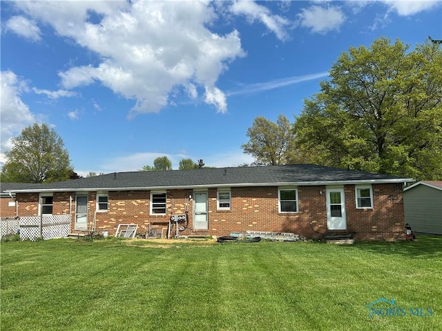 rear view of house with entry steps, brick siding, and a lawn