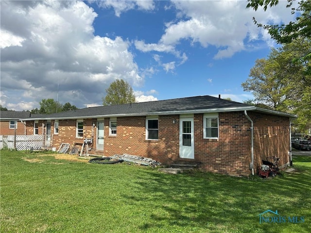 back of property with entry steps, brick siding, and a lawn