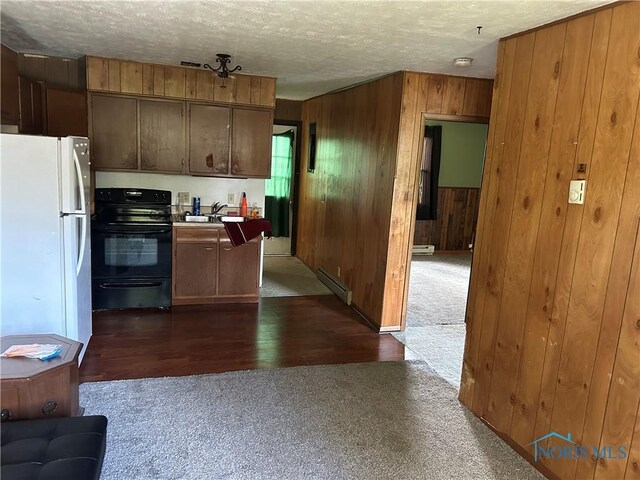 kitchen featuring a sink, wood walls, freestanding refrigerator, black / electric stove, and baseboard heating