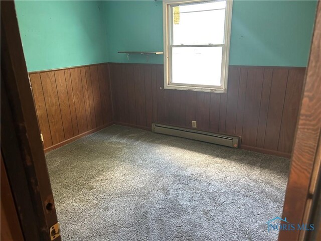 empty room featuring a baseboard radiator, wooden walls, wainscoting, and carpet floors