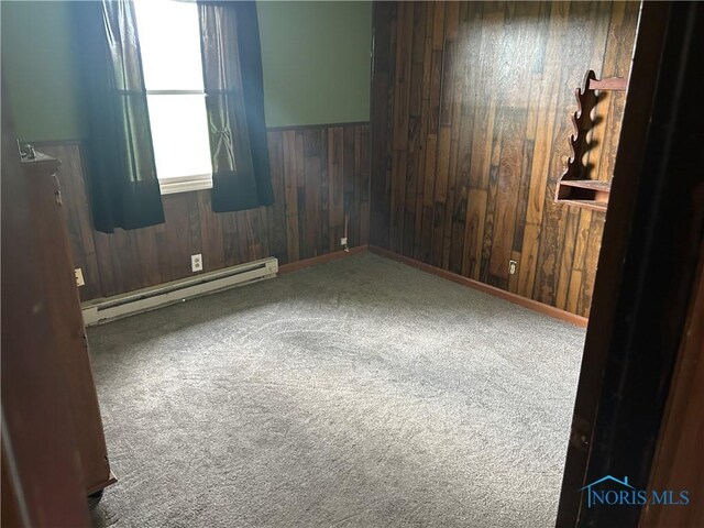 carpeted spare room with a baseboard radiator, wood walls, and wainscoting