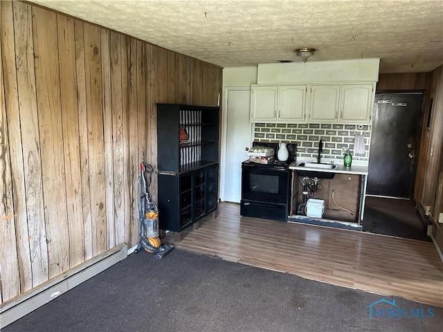 kitchen with carpet, a sink, baseboard heating, black electric range oven, and wooden walls
