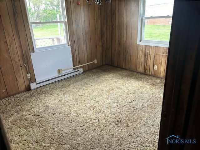 carpeted spare room with a baseboard radiator, wooden walls, a healthy amount of sunlight, and a chandelier