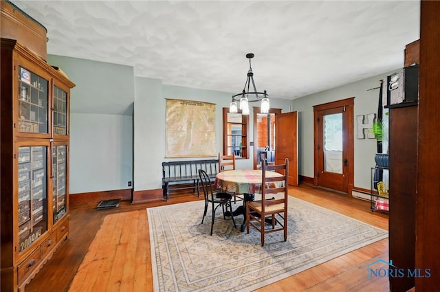 dining space with baseboards, a baseboard heating unit, wood-type flooring, and a notable chandelier