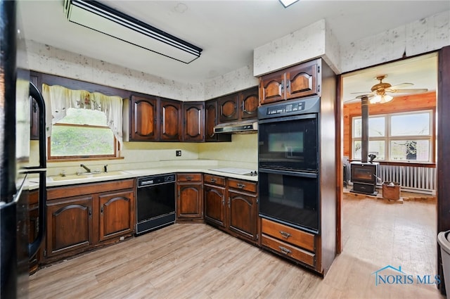 kitchen with light wood-style flooring, a sink, black appliances, a wood stove, and light countertops
