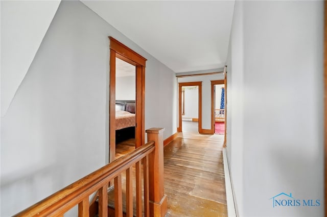 hall with an upstairs landing, light wood-style flooring, baseboards, and a baseboard heating unit