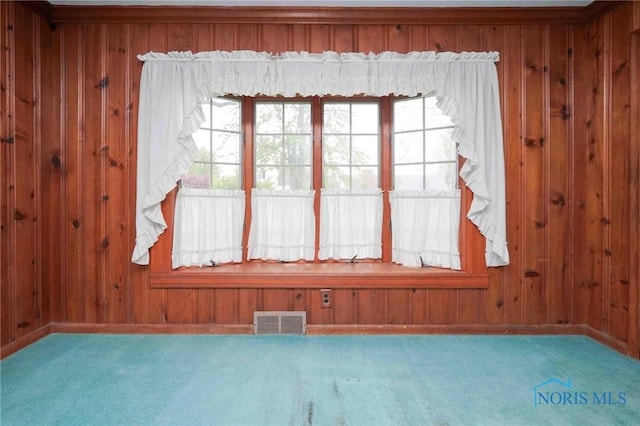 carpeted empty room with wooden walls, a wealth of natural light, and visible vents
