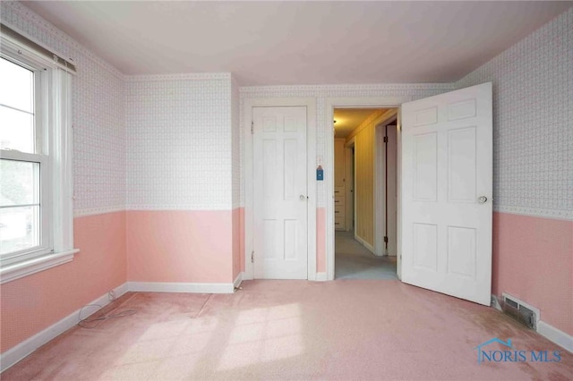 unfurnished bedroom featuring multiple windows, visible vents, and wallpapered walls