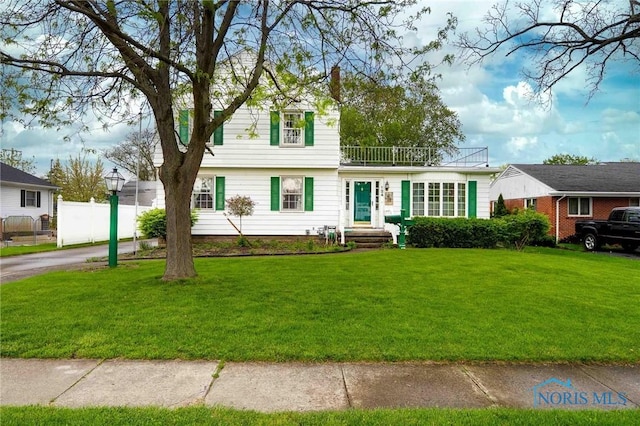 view of front facade featuring a balcony, a front lawn, and fence
