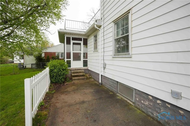 view of property exterior with fence, a balcony, entry steps, a lawn, and a sunroom
