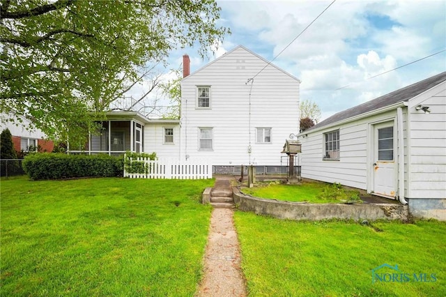 back of property with a sunroom, a chimney, fence, and a lawn
