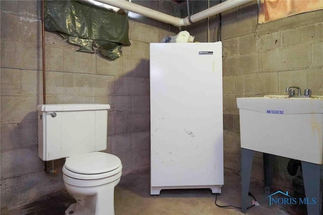half bath with a sink, toilet, and concrete flooring