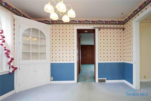 carpeted empty room with a notable chandelier, visible vents, wallpapered walls, and a wainscoted wall
