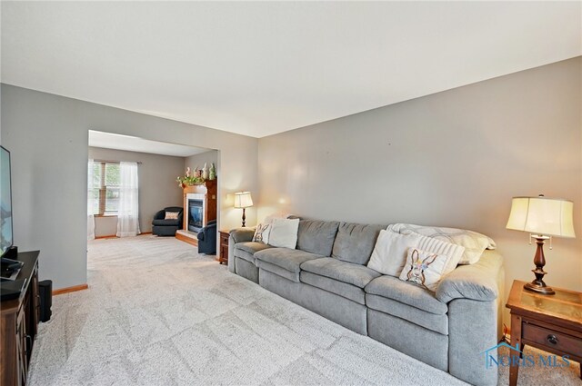 living room featuring baseboards, a glass covered fireplace, and light colored carpet