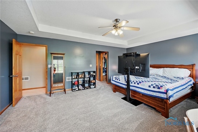 carpeted bedroom featuring a tray ceiling, baseboards, a ceiling fan, and visible vents