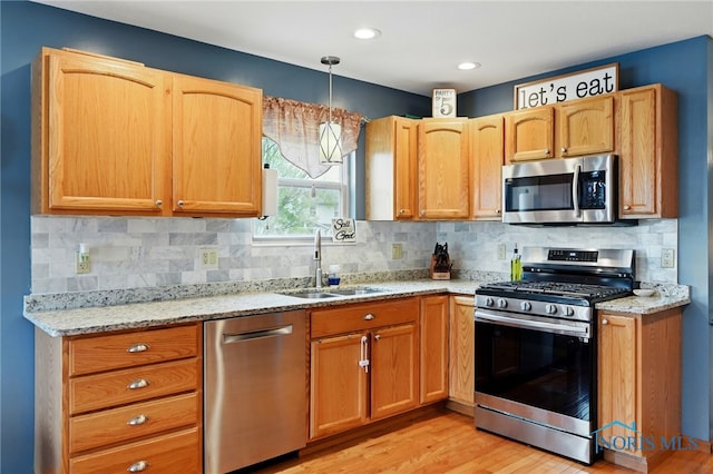 kitchen with light wood-style flooring, light stone counters, a sink, backsplash, and appliances with stainless steel finishes