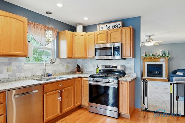 kitchen with light wood-style flooring, a tiled fireplace, ceiling fan, a sink, and stainless steel appliances