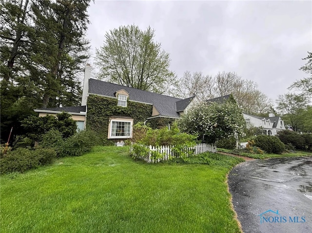 view of front of home featuring fence, roof with shingles, a chimney, and a front yard