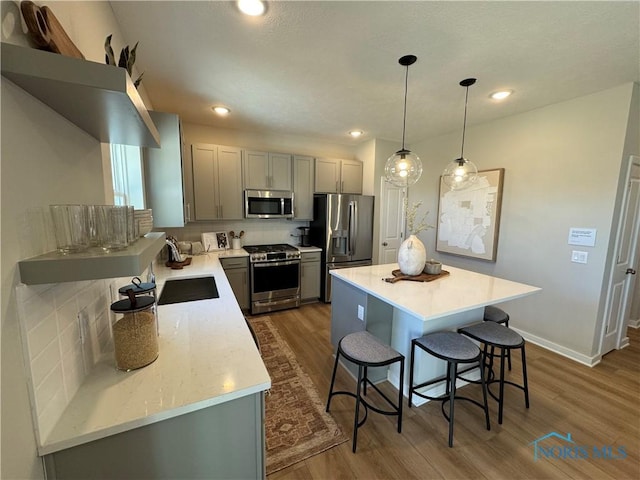 kitchen with a center island, wood finished floors, stainless steel appliances, a kitchen breakfast bar, and gray cabinetry