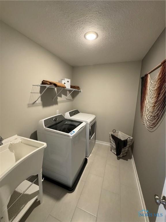 clothes washing area with a sink, laundry area, washing machine and clothes dryer, a textured ceiling, and light tile patterned flooring