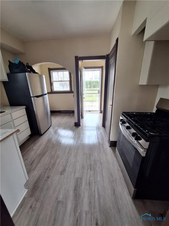 kitchen featuring stainless steel appliances, light wood-style flooring, white cabinetry, light countertops, and arched walkways