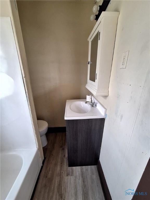 full bathroom featuring toilet, baseboards, a tub to relax in, vanity, and wood finished floors