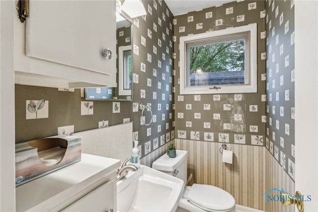 half bathroom with a sink, toilet, and wallpapered walls