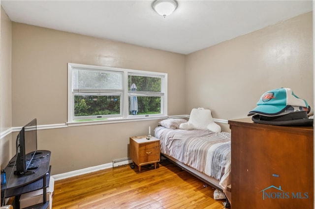 bedroom featuring a baseboard heating unit, hardwood / wood-style floors, and baseboards