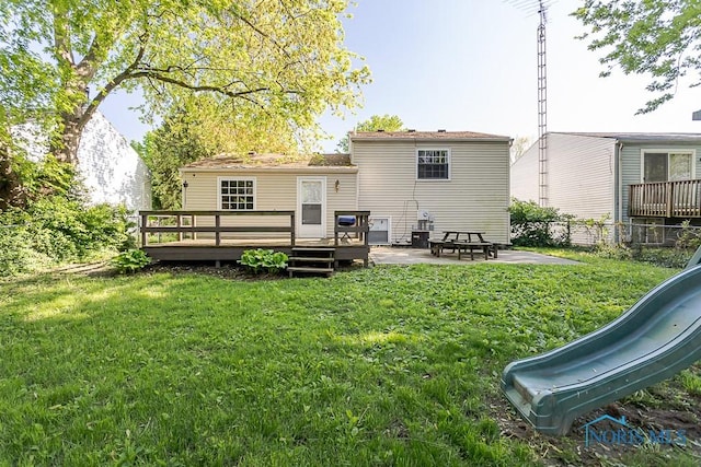 back of house featuring a playground, a yard, a deck, and a patio area