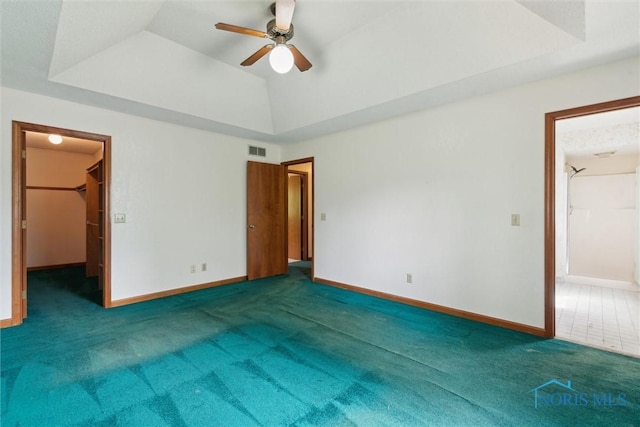 unfurnished bedroom featuring carpet flooring, a walk in closet, baseboards, ceiling fan, and a tray ceiling