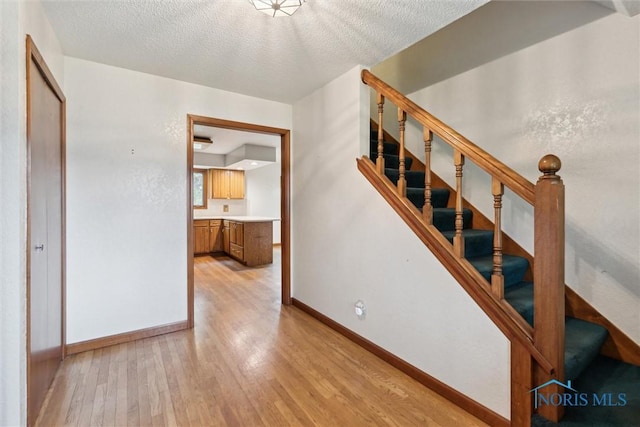 staircase with wood finished floors, baseboards, and a textured ceiling