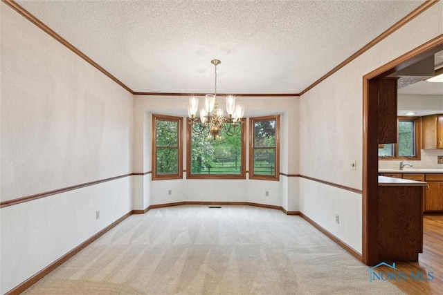 spare room with crown molding, a chandelier, a textured ceiling, light carpet, and baseboards